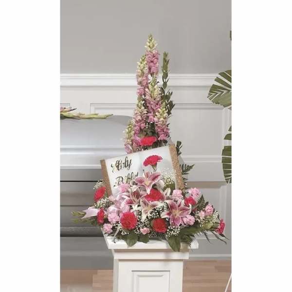Tall floral standing arrangement with a memorial sign and pink lilies