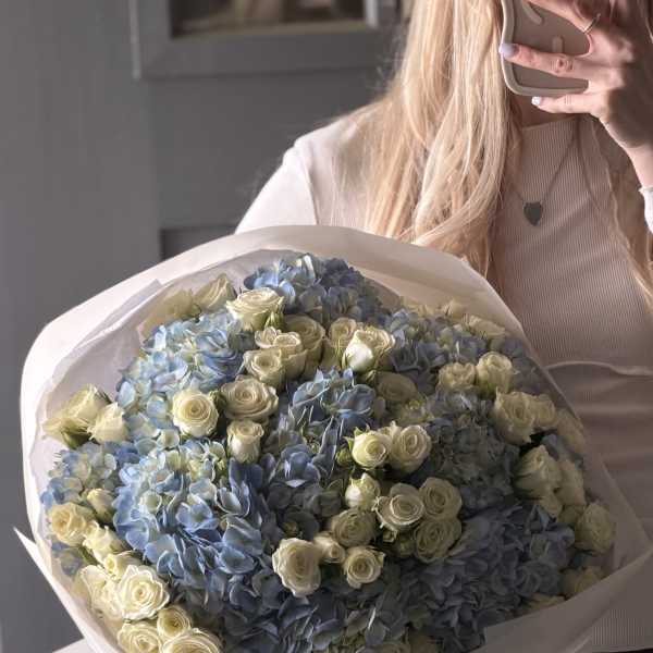 Large bouquet of blue hydrangeas and white roses wrapped in white paper