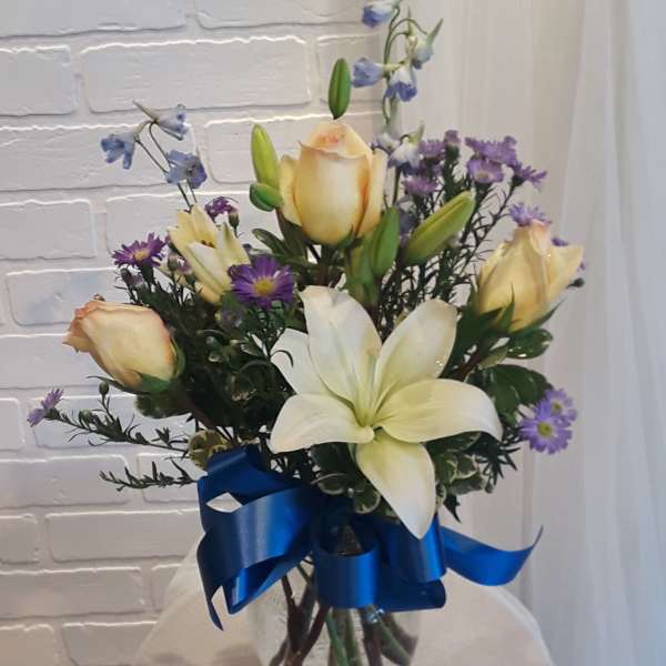Bouquet of white lilies, cream roses, and purple flowers in a glass vase