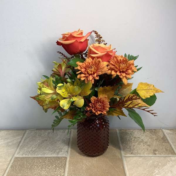 Orange roses and yellow flowers in a brown textured vase