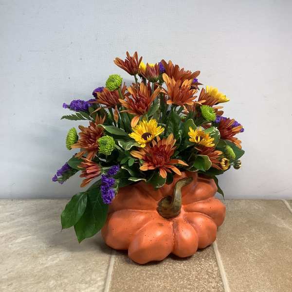 Fall flower arrangement in a pumpkin-shaped container with orange, yellow, and purple blooms