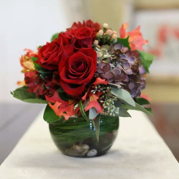 Red roses and hydrangeas arranged in a green glass vase