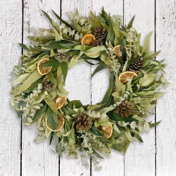 Green wreath with dried orange slices and pinecones on a white wood background