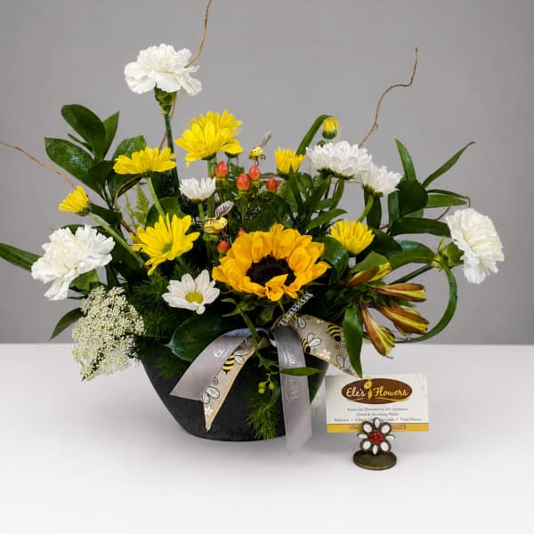 Mixed bouquet with sunflowers, white carnations, and yellow daisies in a black container