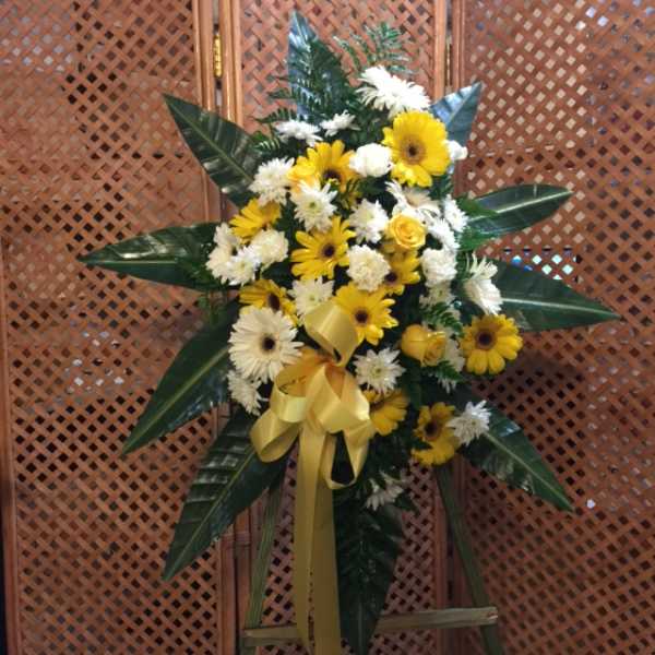 Yellow and white flower spray with a gold ribbon on a stand