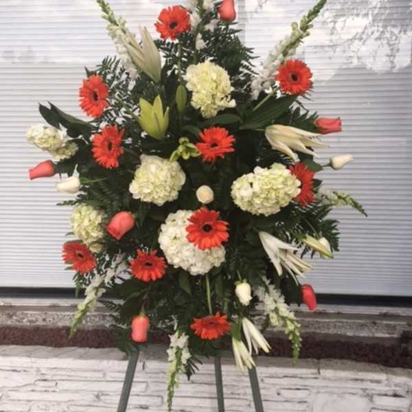 Standing floral spray with red gerberas, white lilies, and pale hydrangeas