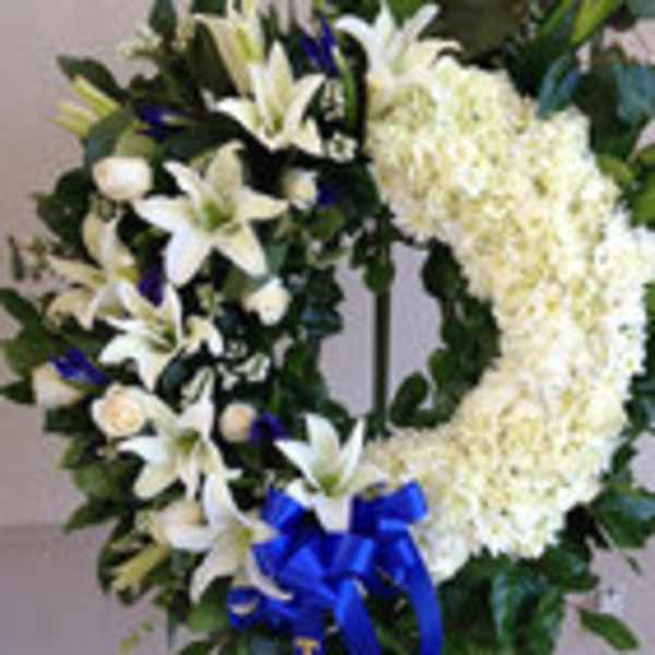 Standing funeral wreath with white lilies, white chrysanthemums, and a blue ribbon