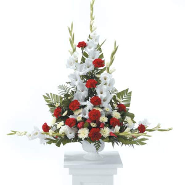 Tall red and white floral spray in a white pedestal vase