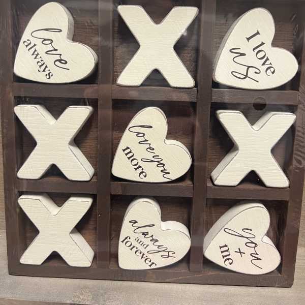 Wooden tic-tac-toe sign with heart and X pieces reading love phrases