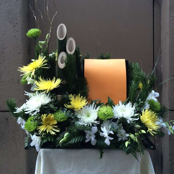 Floral arrangement with yellow and white chrysanthemums around an orange panel