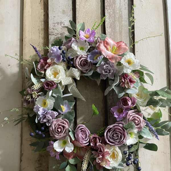 Floral wreath with pink, purple, and white blooms on a rustic wood background