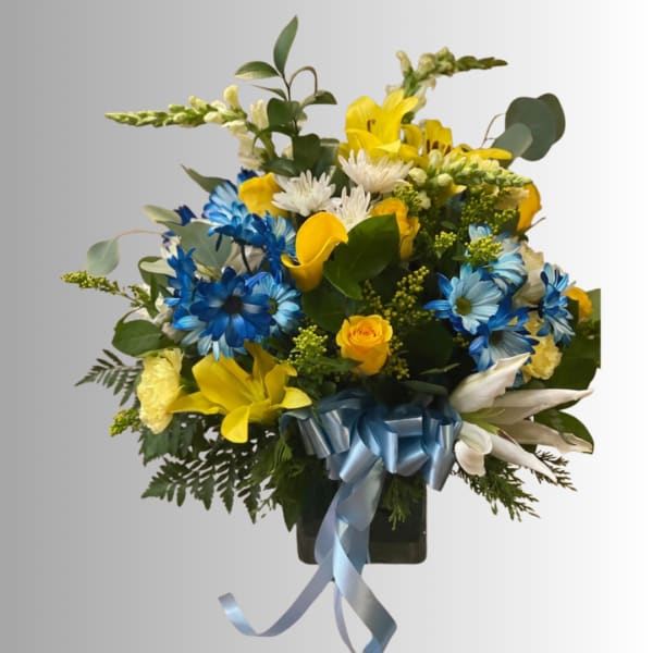 Bouquet of yellow, blue, and white flowers in a dark vase with a blue ribbon