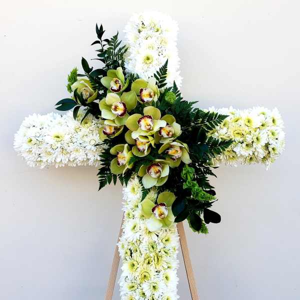 White floral cross with green orchids and dark foliage on an easel