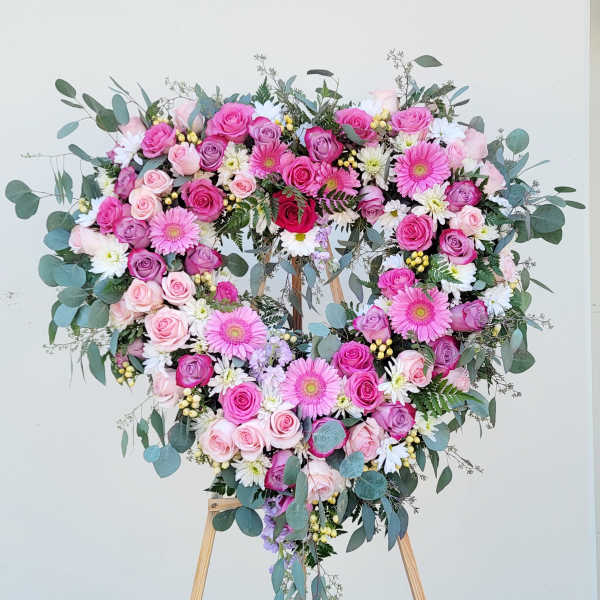 Heart-shaped floral wreath of pink roses and daisies on a wooden stand