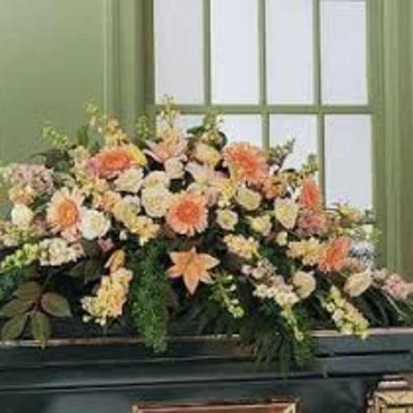 Large peach and white floral arrangement in a dark casket