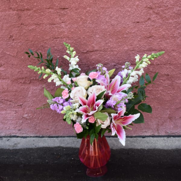 Bouquet of pink lilies, white roses, and purple flowers in a red glass vase
