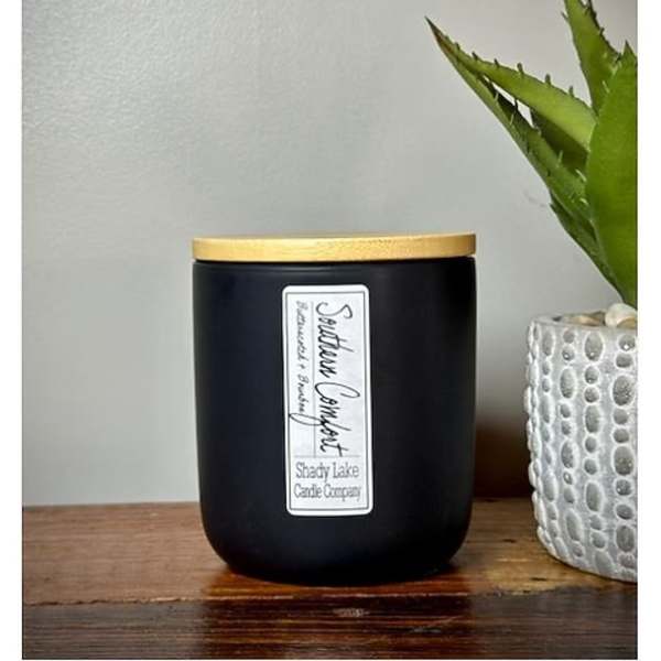 Black candle jar with a gold lid beside a small potted succulent