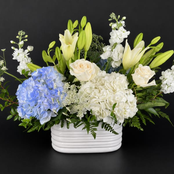 White and blue floral arrangement in a white ceramic vase