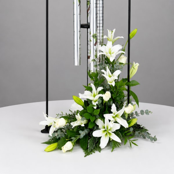 White lilies and roses arranged beneath a black wind chime stand