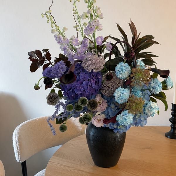 Tall mixed bouquet in a black vase with blue, purple, and white flowers