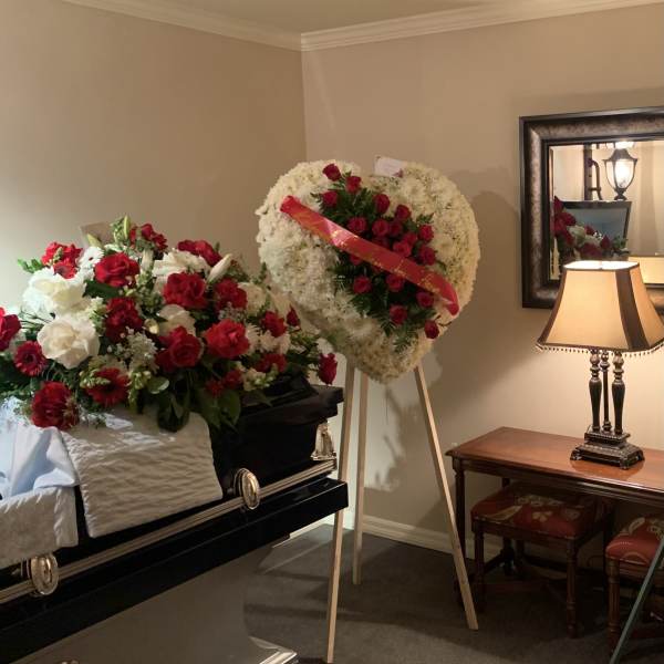 Two floral funeral tributes beside a casket, one on an easel and one draped over the casket.