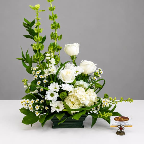 White roses and daisies arranged in a low green container with tall green spikes