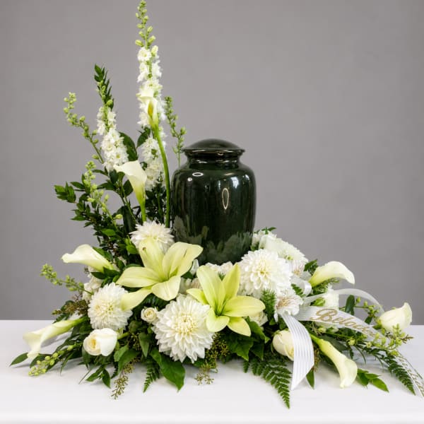 White lilies and mums arranged around a dark green urn