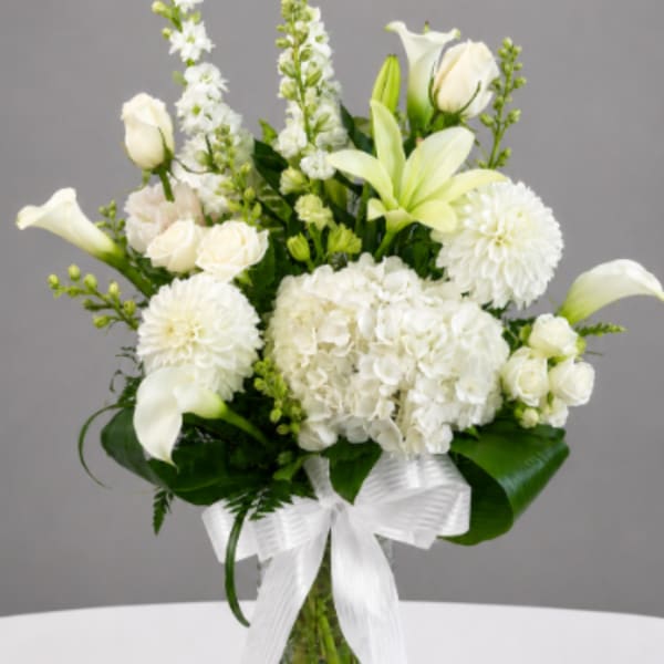 White flowers arranged in a clear glass vase with a white ribbon