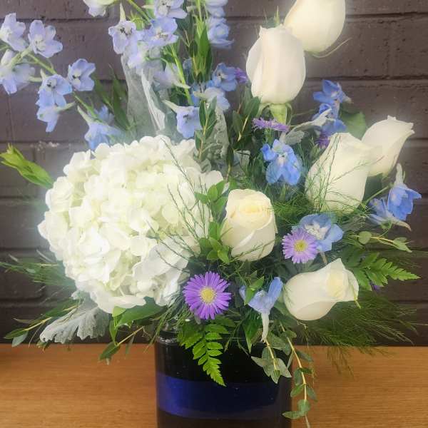 White roses and hydrangea with blue flowers in a dark vase