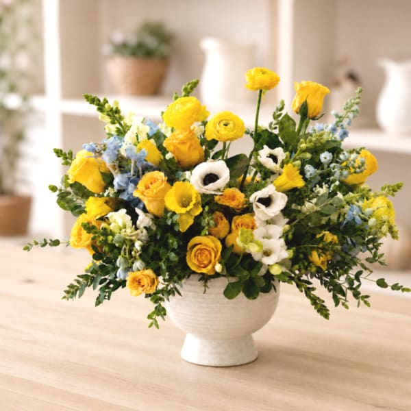 Yellow and white mixed flower arrangement in a white pedestal vase