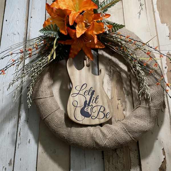 Orange lilies on a burlap wreath with a wooden guitar sign