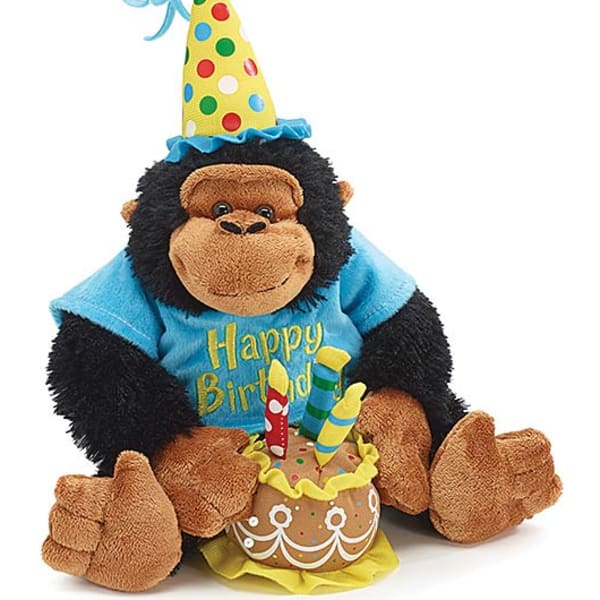 Birthday gorilla plush wearing a party hat and shirt, sitting with a plush cake and candles