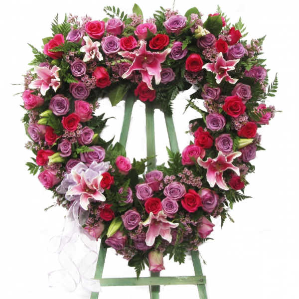Heart-shaped floral wreath on a stand with pink and red roses and lilies