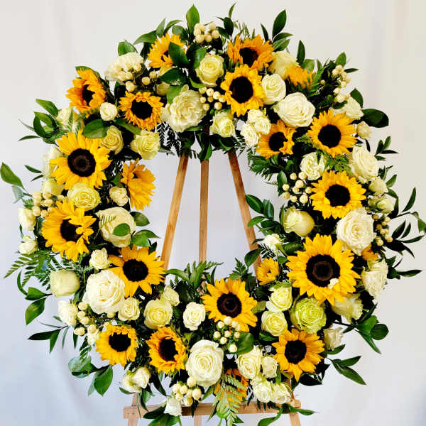 Large floral wreath with sunflowers and white roses on a wooden stand
