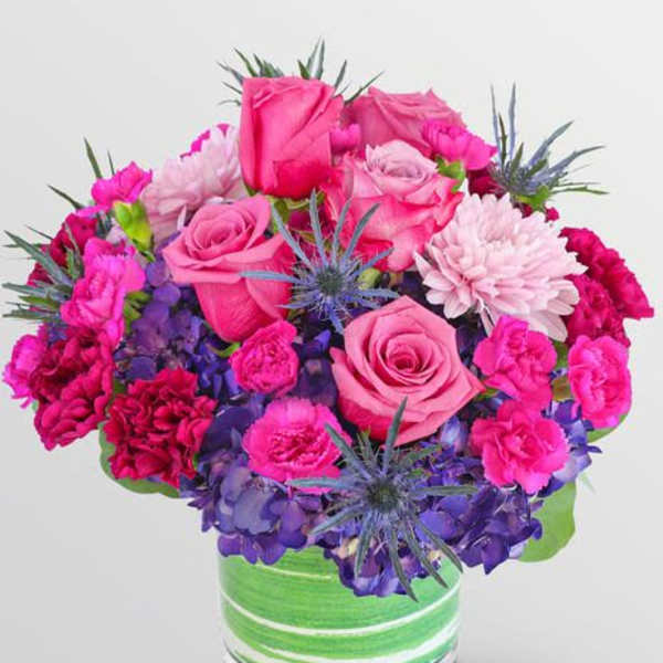 Pink roses and carnations with purple hydrangeas in a green striped vase