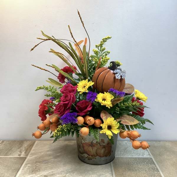 Fall floral arrangement with roses, daisies, and a pumpkin in a decorative container