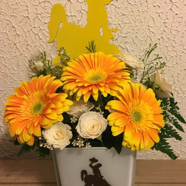 Orange gerbera daisies and white roses in a glass vase with a yellow cowboy topper