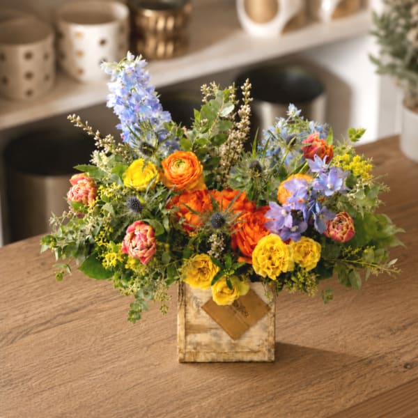 Colorful mixed bouquet in a rustic square vase on a wooden table