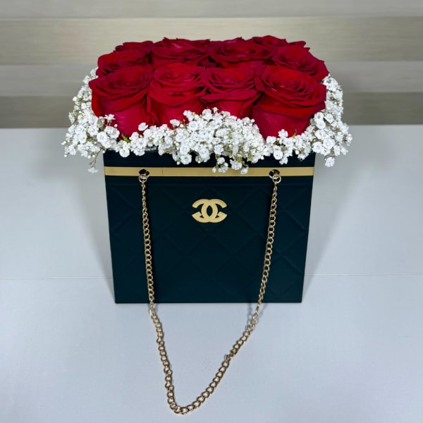 Red roses arranged in a black box with white baby's breath and gold chain handles.