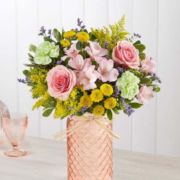 Pink roses and pastel flowers arranged in a peach glass vase