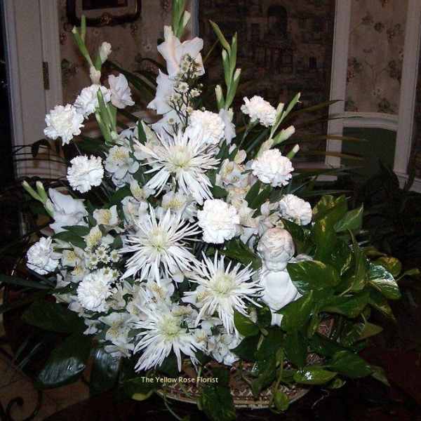 Large white floral arrangement in a basket with a small angel figurine