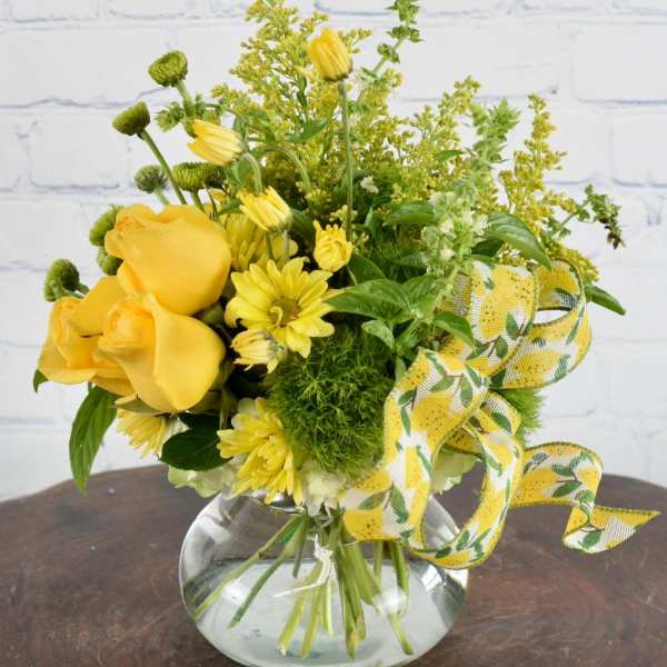 Yellow roses and daisies in a round glass vase with a yellow ribbon