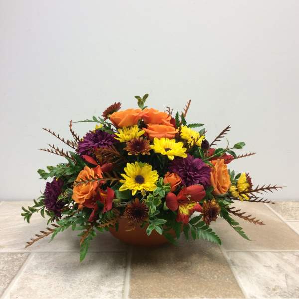 Low floral arrangement with orange roses, yellow daisies, and purple blooms in a bowl vase