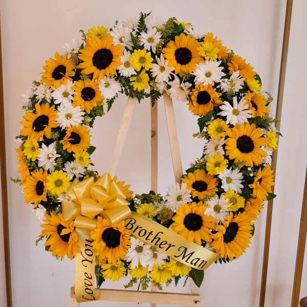 Standing round wreath of yellow sunflowers and white daisies with a yellow bow on an easel