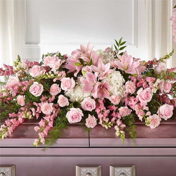 Pink lilies and roses arranged with white blooms on a casket