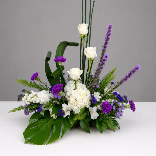 Tall floral arrangement with white roses, purple flowers, and tropical leaves