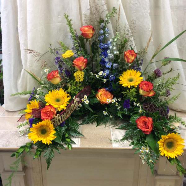 Large floral spray with sunflowers, orange roses, and blue delphinium