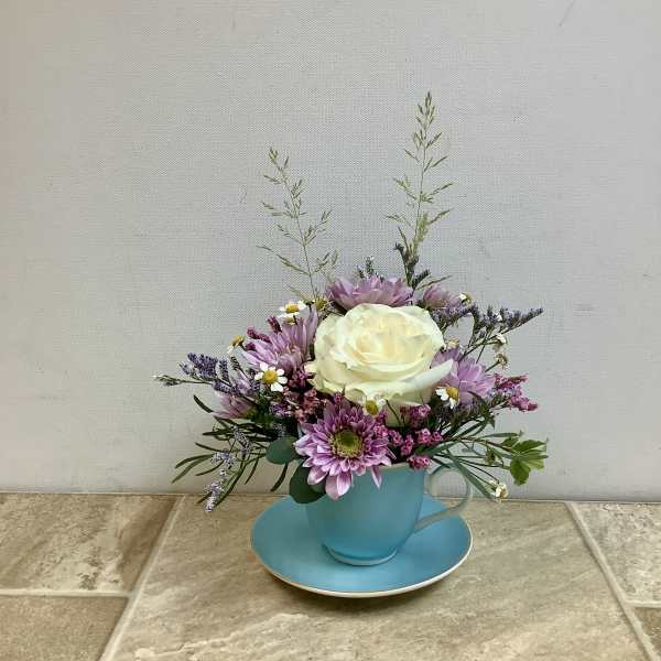Small floral arrangement in a blue teacup and saucer with pink and white blooms