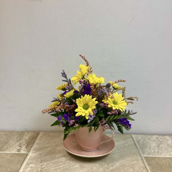 Yellow daisy bouquet in a pink teacup and saucer