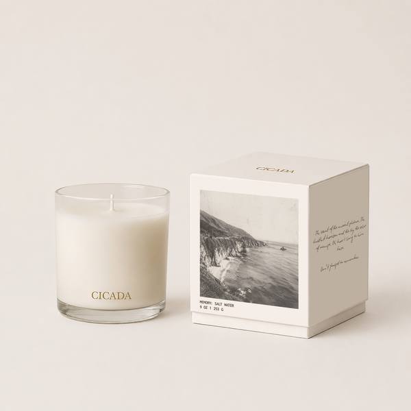 White candle in a glass tumbler beside a boxed candle